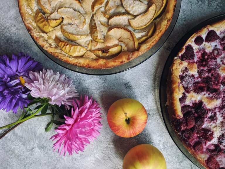 Top-down view of homemade apple and raspberry pies with colorful flowers.