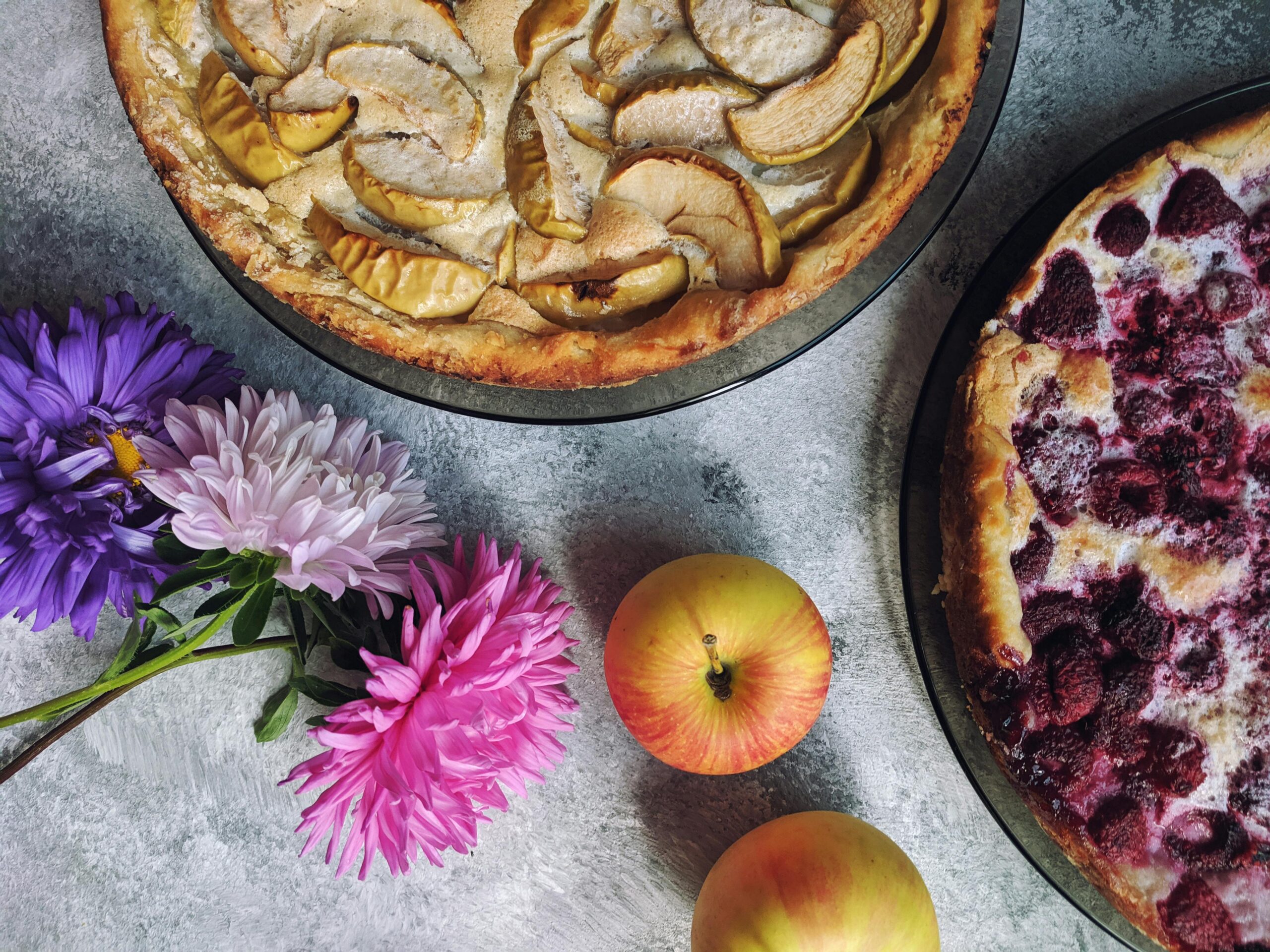 Top-down view of homemade apple and raspberry pies with colorful flowers.