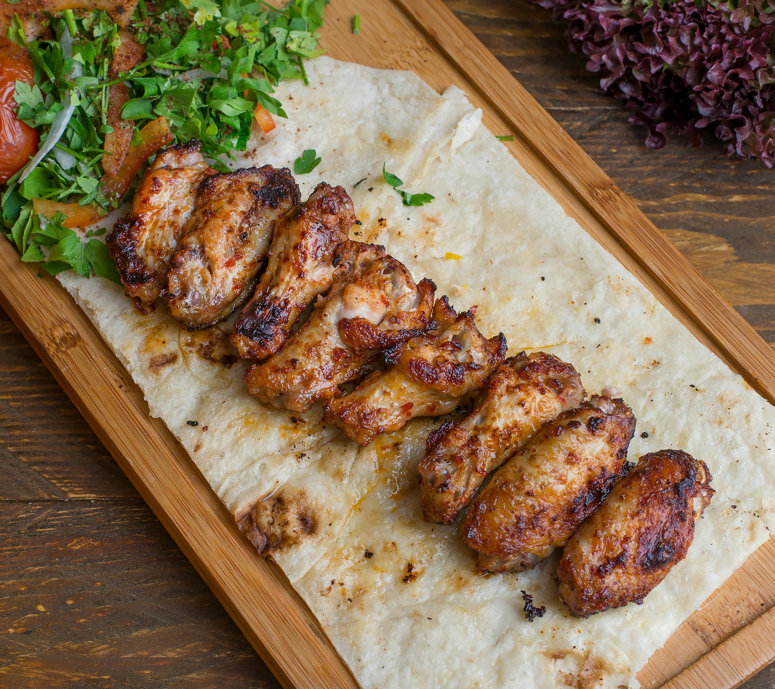 Delicious grilled chicken wings served on flatbread with fresh herbs and vegetables.