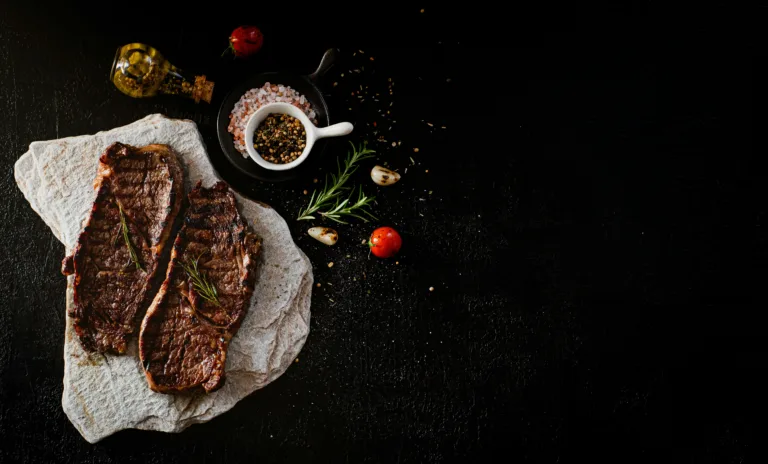 Delicious grilled steak served with rosemary, garlic, and spices on a stone slab, perfect for a gourmet meal.