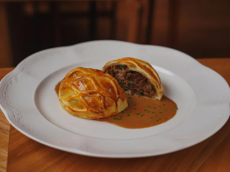 Close-up of freshly baked Beef Wellington with sauce on a white plate.