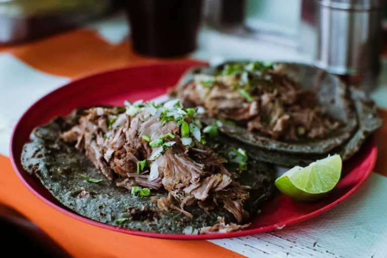 Close-up of delicious barbacoa tacos on a red plate with fresh lime in Ciudad de Mรฉxico.