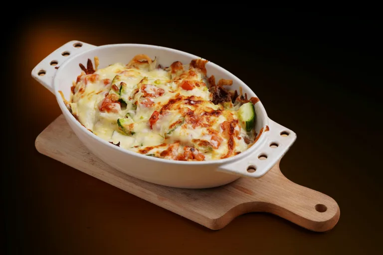 Delicious baked vegetable casserole topped with cheese in a white dish on a wooden board.