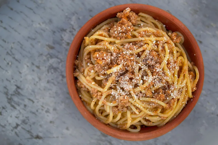 Delicious homemade spaghetti with meat sauce and parmesan served in a rustic bowl.