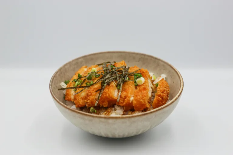 A mouthwatering chicken katsu served on steamed rice with savory toppings in a bowl.